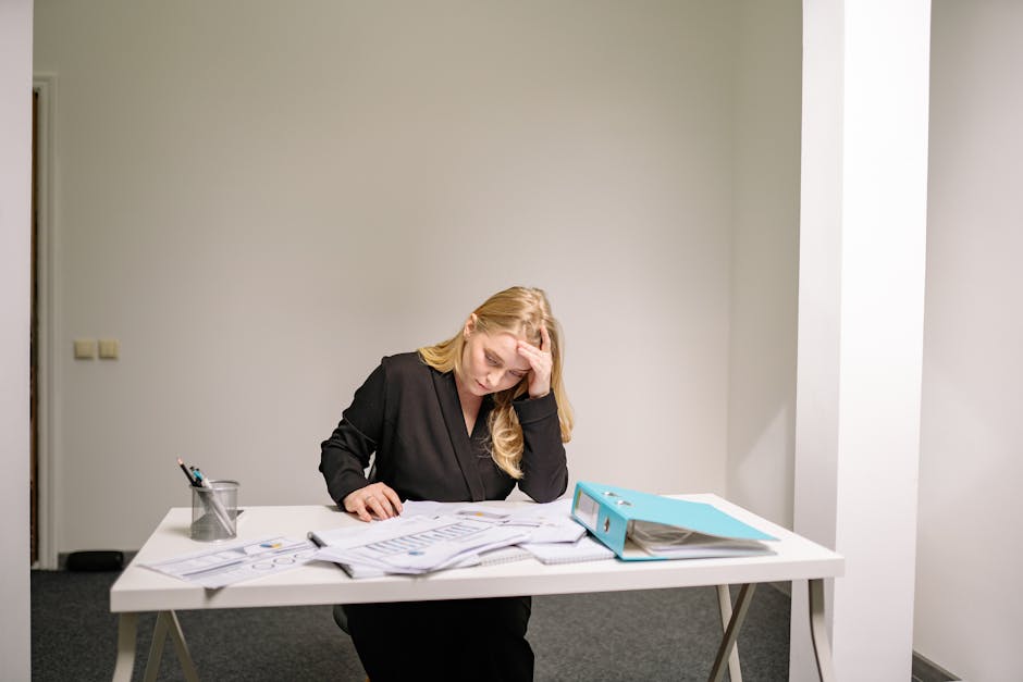 A woman in professional attire doing a gentle yoga stretch at her office desk to relieve tension.
